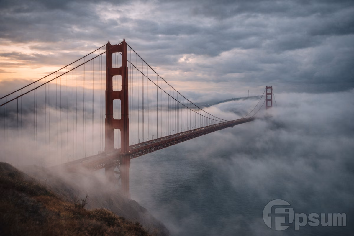 Golden Gate Bridge stretching across San Francisco Bay with rolling coastal fog and dramatic cloudy skies at sunrise.